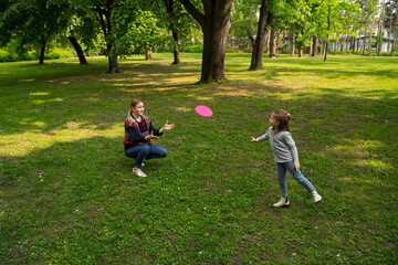 Cute little 5 year old girl playing frisbee with her mom in the park 