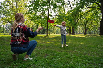 Cute little 5 year old girl playing frisbee with her mom in the park 