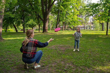 Cute little 5 year old girl playing frisbee with her mom in the park 