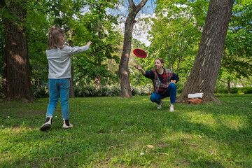 Cute little 5 year old girl playing frisbee with her mom in the park 