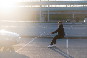 Caucasian man pulling a car with a rope. 