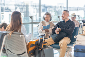 happy asian senior family waiting for boarding in the airport terminal,enjoy talking together,elderly woman taking note something on notebook