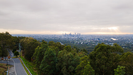 Brisbane skyline emerging from lush forest at sunrise under cloudy sky