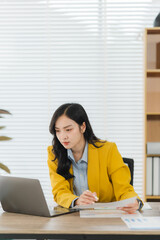 Focused Professional at Work: A young businesswoman in a bright yellow blazer is deeply focused,...
