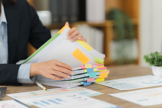 Analyzing Documents: A focused individual, meticulously reviewing a vibrant stack of important papers, documents, and charts, ensuring careful attention to detail and thoughtful preparation.