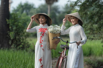 Beautiful Vietnamese Asian woman wearing White color Ao Dai National Costume Dress with red bicycle in rice fields. Portrait fashion show in nature.