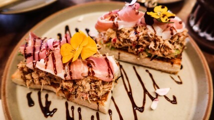 close up of a toast with tuna and ham, decorated with edible flower on top and with vinegar suace 
