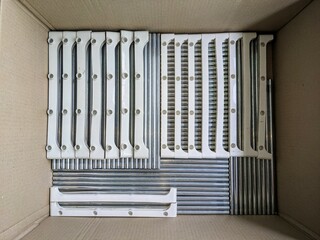 Metal rods and plastic components of a disassembled shelf, tidily arranged in a box. Organization and storage concept.