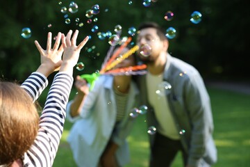 Family holiday getaway. Parents and daughter playing with soap bubbles outdoors, selective focus