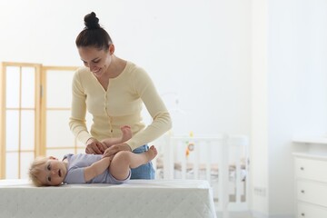 Mother playing with her cute baby on changing table at home, space for text