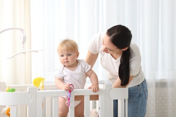Mother playing with her cute baby in crib at home