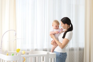 Mother with her little baby near crib at home