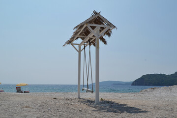 Charming Beach Swing with Thatched Roof on a Scenic Montenegro Beach, Overlooking the Adriatic Sea...
