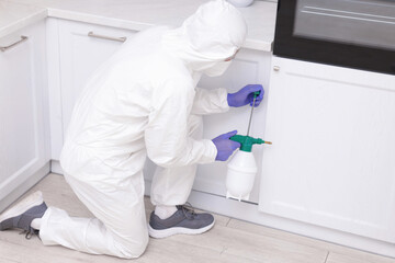 Pest control worker in protective suit spraying insecticide at home