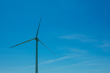Wind turbine is standing tall in the sky. The sky is clear and blue. The wind turbine is the only object in the image.