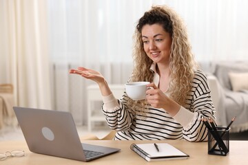Smiling woman having videochat by laptop at desk in home office