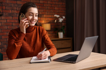 Smiling woman talking by smartphone and working at desk in home office