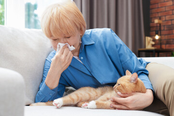Senior woman suffering from allergy with her cat on sofa at home