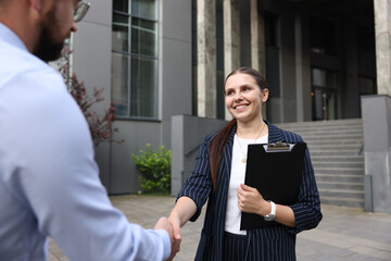 Happy coworkers shaking hands near office building