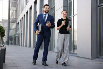 Happy coworkers with smartphone and coffee discussing something near office building