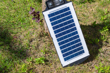 Solar panel is sitting on the grass. The panel is black and blue. The grass is green and the ground is brown.