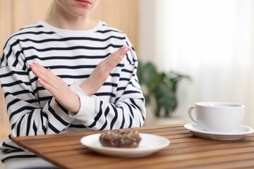 Gluten free diet. Woman refusing from donut at wooden table indoors, closeup