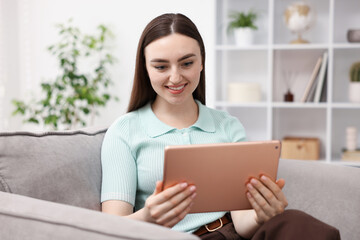 Fototapeta premium Young woman using modern tablet in armchair at home