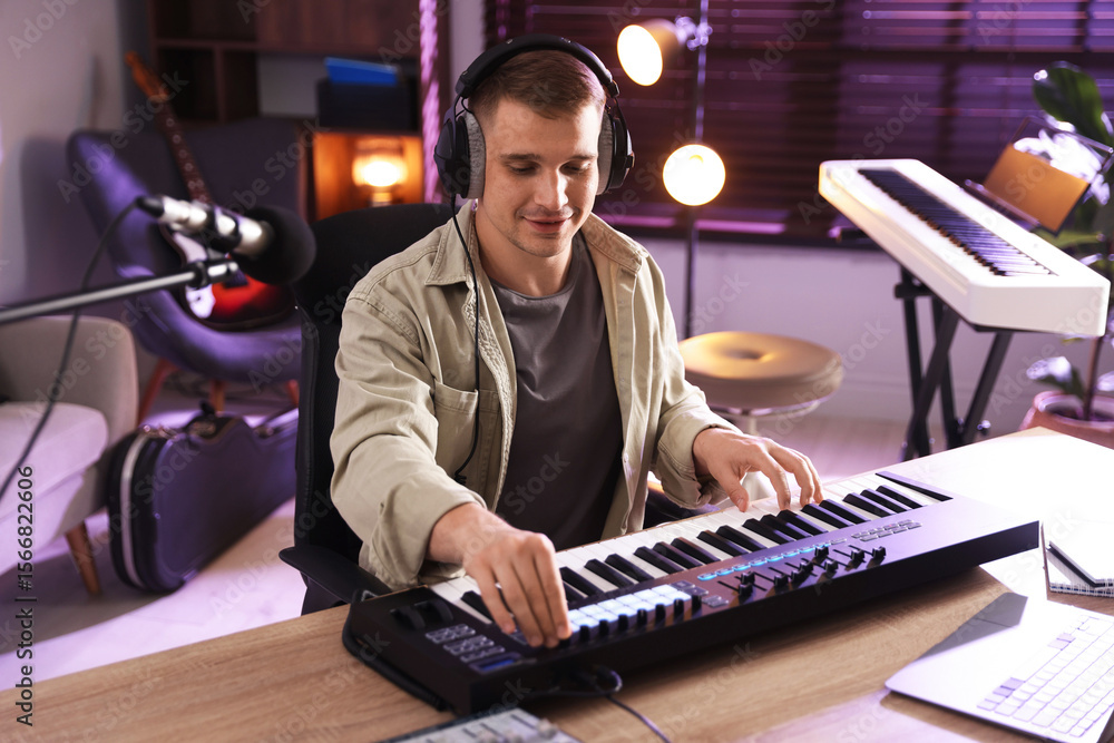 Poster man in headphones working with midi keyboard at table in home studio