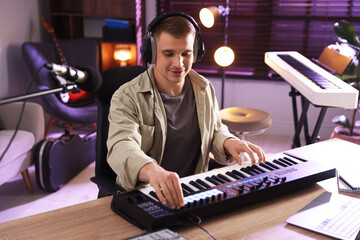 Man in headphones working with MIDI keyboard at table in home studio