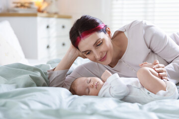 Mother putting her cute newborn baby to sleep on bed at home
