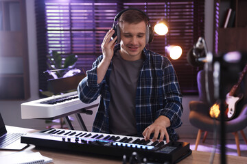 Smiling man in headphones working with MIDI keyboard at table in home studio