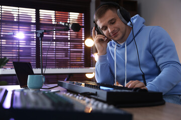 Man in headphones working with MIDI keyboard at table in home studio, low angle view