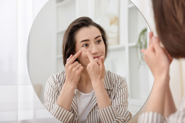 Woman putting in contact lens near mirror indoors