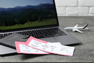 Passport, flight tickets, plane model and laptop on grey table, closeup