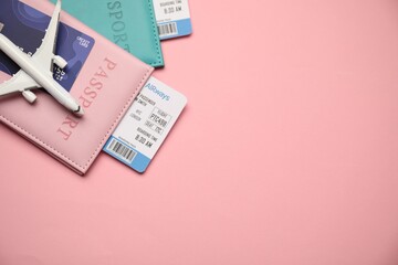 Passports with tickets, credit card and airplane model on pink background, top view. Space for text