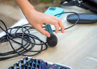 Hand reaching for a wired microphone on a wooden table with audio cables and a mixer. Concept of...