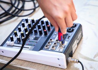 Close-up of a hand plugging audio cable into sound mixer, with visible knobs and inputs. Concept of...