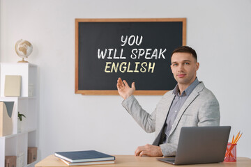 Teacher pointing at text You Will Speak English on black chalkboard in classroom. Language course