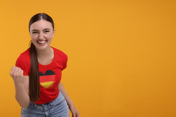 Excited fan with flag of Germany on her t-shirt against orange background. Space for text