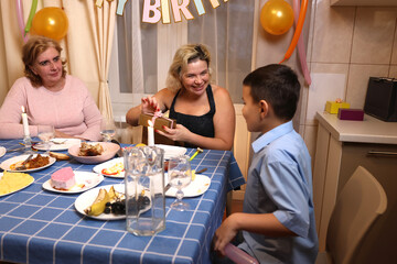 A woman with her son, sister, and nephew celebrates a birthday at a festive table. Soft lighting.