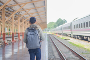 Young man standing alone at sunrise, standing on train station platform, holding map, confused but...