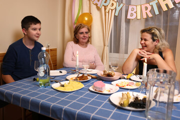 A woman with her son, sister, and nephew celebrates a birthday at a festive table. Soft lighting.