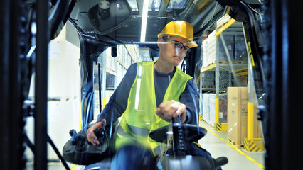 First-person view of a warehouse worker in a yellow vest and helmet operating a forklift through busy aisles, showcasing precision and care in global supply chain management. © stockcopter