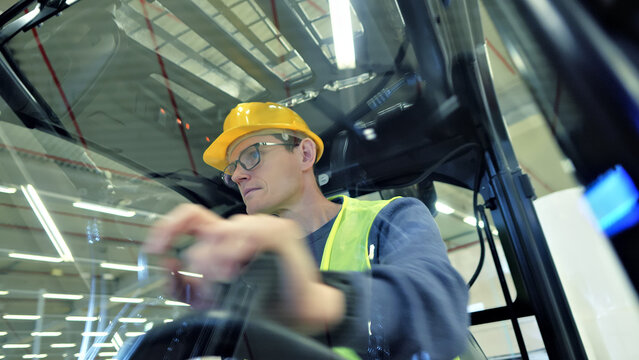 Industrial operator in yellow hard hat and safety vest skillfully maneuvers a forklift in a vast warehouse, ensuring efficient cargo management and seamless logistics.