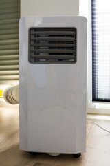 A portable white air conditioner on wheels, with an exhaust hose connected to the window