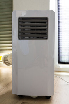 A portable white air conditioner on wheels, with an exhaust hose connected to the window