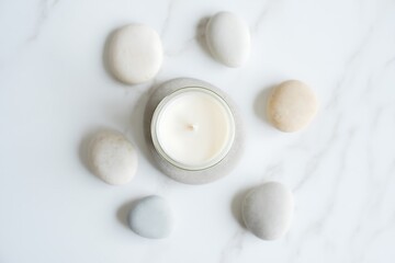 Beautifully Arranged White Candle Surrounded by Smooth Natural Stones on a Clean White Marble Surface Creating a Serene and Peaceful Aesthetic for Relaxation and Home Decor