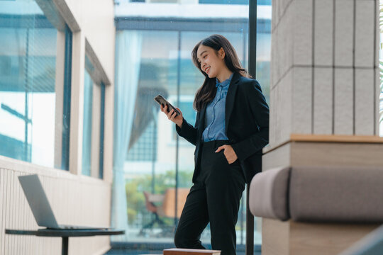 Businesswoman using smartphone in modern office building lobby - Powered by Adobe