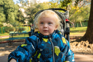 A baby is sitting in a stroller with a blue jacket on
