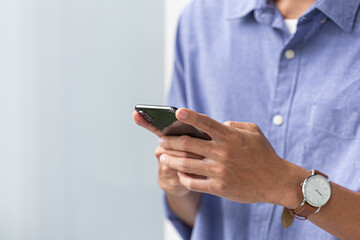 Midsection of a man in casual blue shirt holding smartphone and typing, perfect for modern lifestyle, mobile communication, and digital work themes.